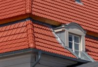 Tradition in rotbraun auf Mehrfamileinhaus mitten in der Stadt - der Dachziegel von Jacobi im Doppelmuldendesign. Im Bildfokus der  formschöne Gradanfänger in Muschelform aus dem keramischen Jacobi-Zubehör