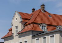 De dakpan Tradition in roodbruin op een appartementencomplex midden in de stad – de keramische dakpan van Jacobi met het karakteristieke dubbelholle profiel. Op de foto ligt de nadruk op de schildkap met voetwolf en de fraaie erker.