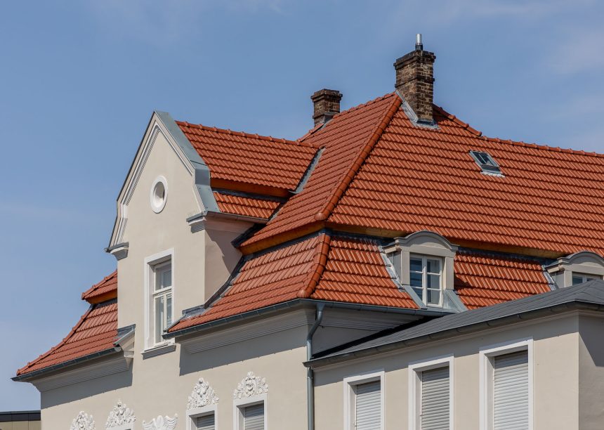 De dakpan Tradition in roodbruin op een appartementencomplex midden in de stad – de keramische dakpan van Jacobi met het karakteristieke dubbelholle profiel. Op de foto ligt de nadruk op de schildkap met voetwolf en de fraaie erker.