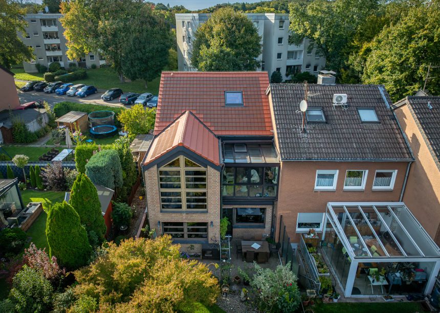 PV-oplossing met zonnepannen in roodbruin – het volledige referentieproject van een hoekrijwoning, gefotografeerd met een drone.