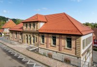 Straataanzicht van een door Zipperlein Holzbau gerenoveerd vakwerkhuis met zandstenen en klinkerelementen, gedekt met Tradition in natuurrood.