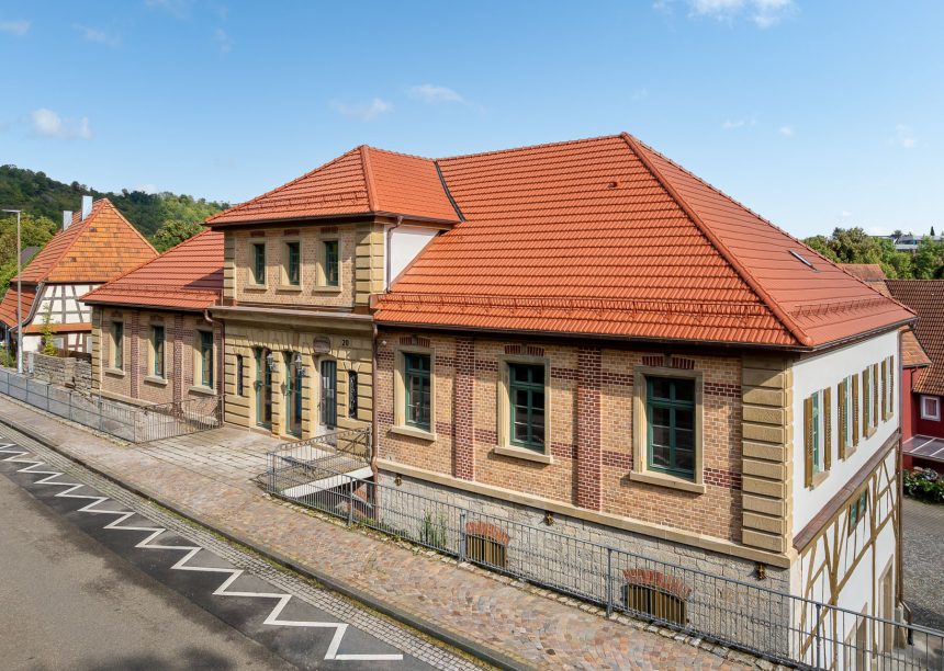Straataanzicht van een door Zipperlein Holzbau gerenoveerd vakwerkhuis met zandstenen en klinkerelementen, gedekt met Tradition in natuurrood.